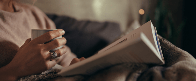 Tasse de thé, plaid et livre posé dans un coin lecture cosy, ambiance parfaite pour une journée de lecture immersive et relaxante.