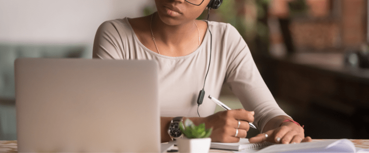 Autrice concentrée écrivant dans un carnet face à son ordinateur, casque sur les oreilles, symbole d’une session d’écriture rapide et efficace.