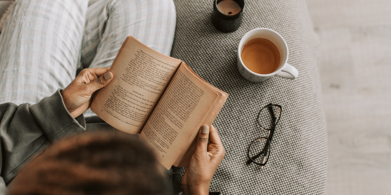 Personne lisant un livre ancien avec une tasse de thé et une bougie allumée, ambiance cosy et automnale idéale pour des lectures doudous en octobre.