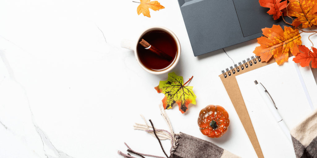 Bureau d’automne cosy avec carnet, stylo, tasse de thé à la cannelle, plaid et feuilles d’érable décoratives – ambiance Halloween créative et réconfortante.